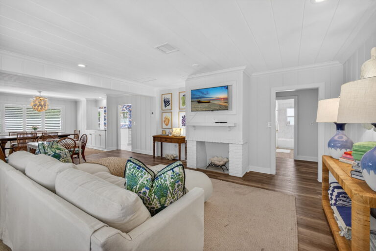 Living room view toward white brick fireplace with wall-mounted TV, wooden console table, botanical wall art, and light wood flooring.