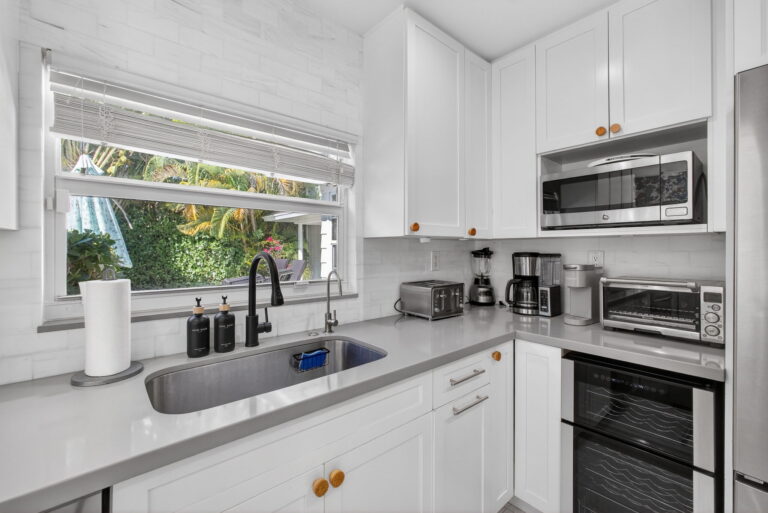 Kitchen sink area with undermount stainless steel sink, black faucet, white subway tile backsplash, and window with white blinds.