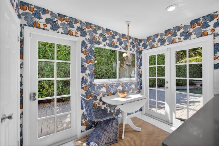 Breakfast nook with blue and orange floral wallpaper, white pedestal table, blue wicker chairs, and French doors opening to the patio.