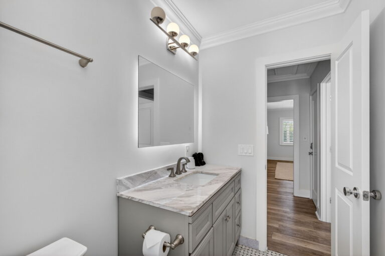 Bathroom vanity close-up with marble countertop, brushed-metal faucet, mirror, and open door to hallway with wood-look floors.
