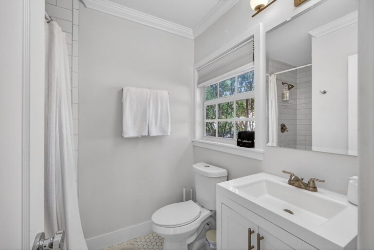 Bathroom view with white vanity, toilet, shower with white curtain, and white subway tile in shower area.