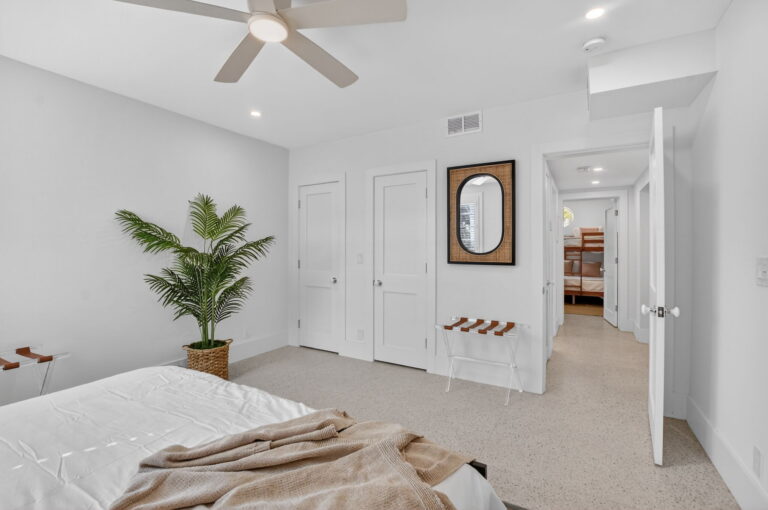 Bedroom view toward white closet doors and open hallway, with oval rattan mirror, luggage rack, and bunk beds visible beyond.
