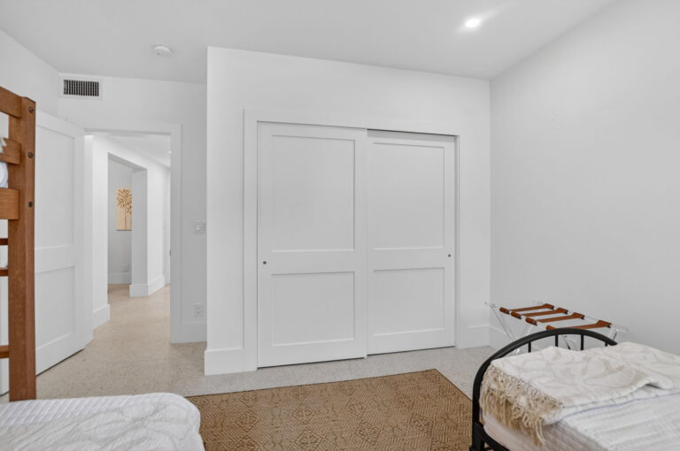 Bedroom view toward white sliding closet doors and open hallway, with metal luggage rack and twin bed in foreground.