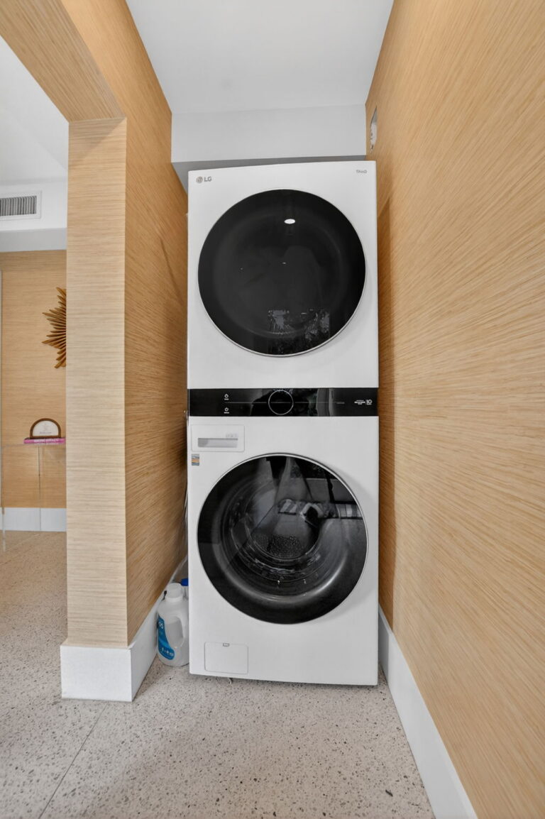 Compact laundry nook with stacked white LG washer and dryer, wood-textured wallpaper, and terrazzo flooring.