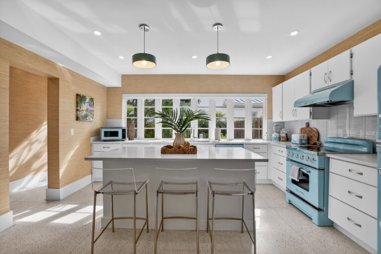 Bright modern kitchen with white cabinetry, waterfall island, clear acrylic bar stools, and light blue retro-style range and appliances.