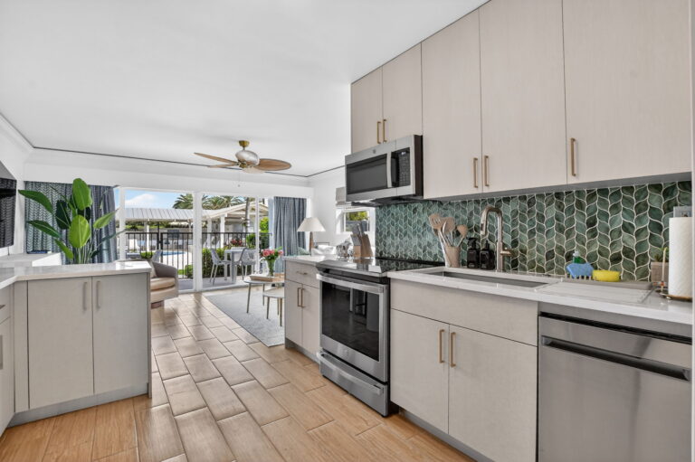 Kitchen workspace with stainless steel oven, microwave, dishwasher, green scalloped backsplash, and open view to private patio through living room.
