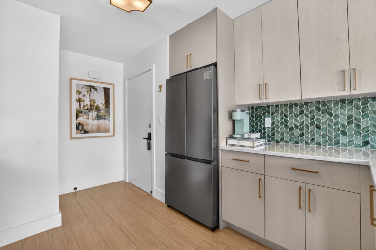 Kitchen with built-in stainless refrigerator, white cabinetry, palm tree hallway art, and doorway to adjacent room.
