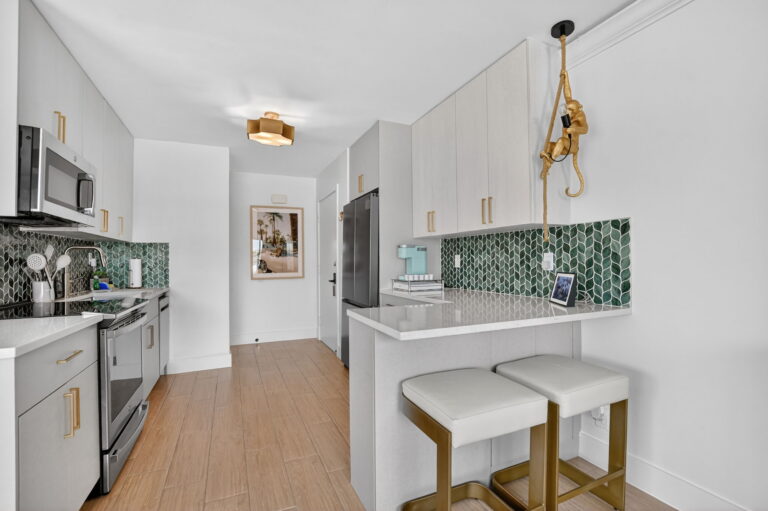 Modern kitchen with green scalloped tile backsplash, white cabinets, gold hardware, breakfast bar, and gold monkey accent decor.