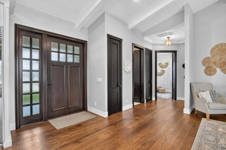 Entry foyer with dark wood front door, hardwood floors, vaulted ceiling, and interior hallway.
