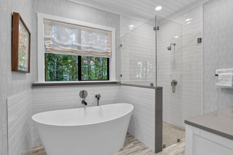 Bathroom with freestanding soaking tub, subway tile shower with glass enclosure, patterned wallpaper, and window with garden view.