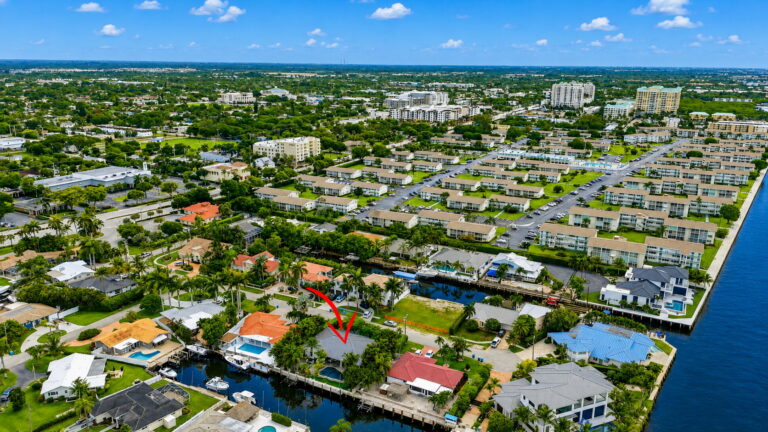 Wider aerial from the canal highlighting the home with backyard, dock access, surrounding waterways, and nearby condo buildings.