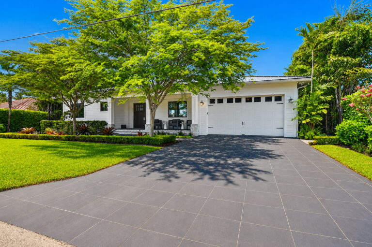 Wide driveway to white garage, front lawn, and white home with black window accents.