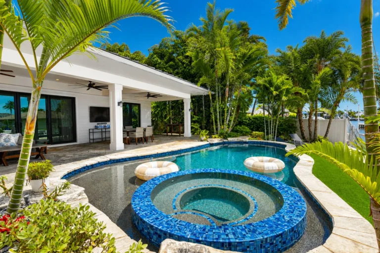 Pool and spa with blue tile, sun shelf, and view to covered patio with outdoor dining, wall-mounted TV, and sliding doors.