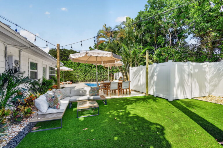 Turf yard with white sectional sofa, dining table, string lights, and a view toward the pool and patio area