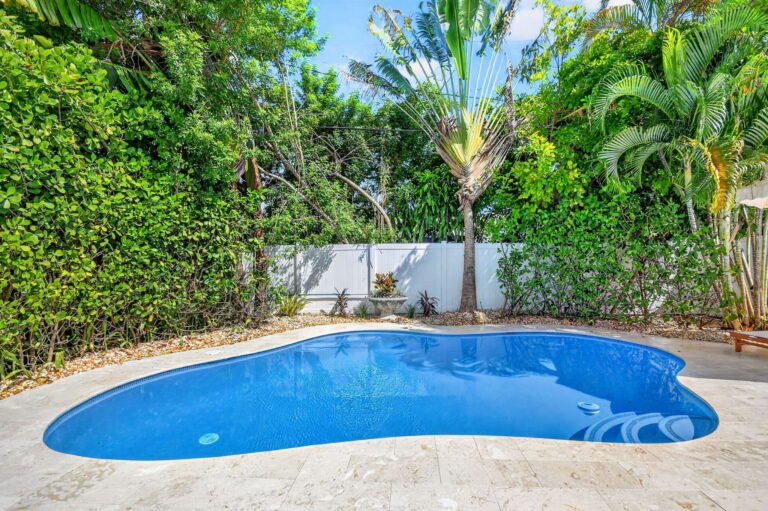 Free-form swimming pool surrounded by dense tropical landscaping, palm trees, and a travertine deck